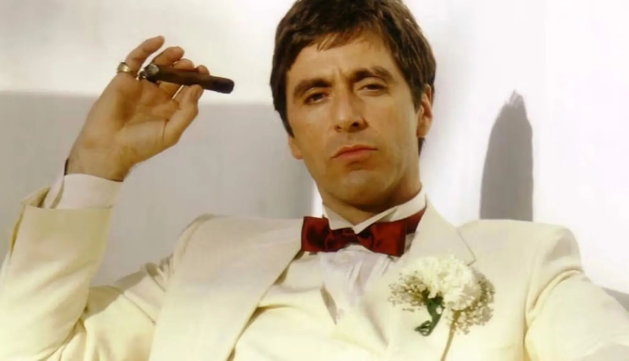 Man in a cream tuxedo and red bow tie holding a cigar